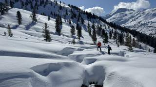 Frau und Mann auf Tourenski passieren einen tief verschneiten Wasserlauf