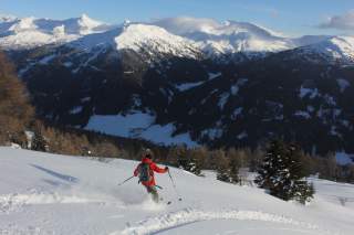 Mensch bei der Abfahrt durch Tiefschnee mit Blick auf die Berge und ins Tal