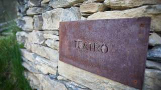 Schild aus Cortenstahl mit der Aufschrift „TEATRO“ an einer Steinmauer befestigt.