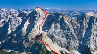Berglandschaft mit markantem Gipfel; ein roter Pfad markiert den Aufstieg vom Tal zum Gipfel.