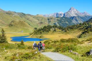 Zwei Seniorinnen und zwei Senioren beim Wandern auf leichten Wegen in einem schönen Hochtal, im Hintergrund ein See.