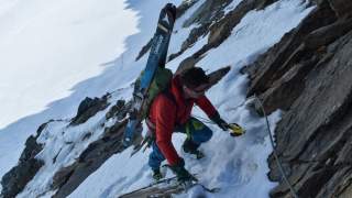 Mensch mit Ski am Rucksack klettert seilversicherte Stelle hinauf
