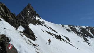 Mensch mit Ski am Rucksack quert schneebedeckten Hang