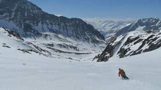 Skifahrer fährt Berg hinab mit Ausblick über schneebedeckte Gipfel