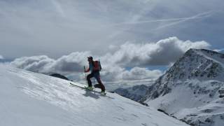 Mensch geht mit Tourenski steilen Schneehang hinauf