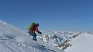 Skifahrer bei Abfahrt mit Blick über verschneite Berggipfel