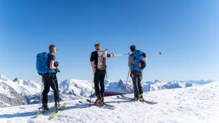 Drei Männer auf Tourenski schauen auf umliegende Gipfel