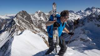 Mann trägt Ski beim Gipfelaufstieg