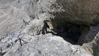 Felsiger Bergpfad mit verbogenen Metallseilen als Sicherung, im Hintergrund Geröll und Felsen.