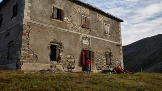 Wandergruppe mit Ausrüstung vor einem verfallenen Berghaus