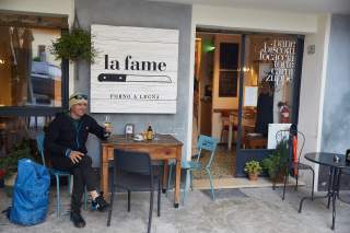 Ein Mann sitzt an einem Holztisch vor einer Bäckerei mit dem Schild 
