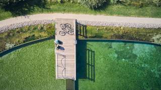 Luftaufnahme: zwei Menschen sitzen auf Steg in grün-blauem See