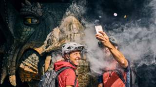 Zwei Menschen machen Selfie vor großem Drachen aus Holz