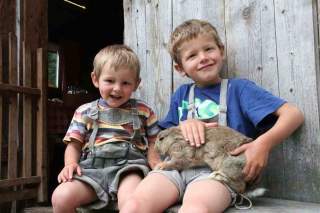 Zwei Kinder sitzen auf Bank und haben Kaninchen auf dem Schoß