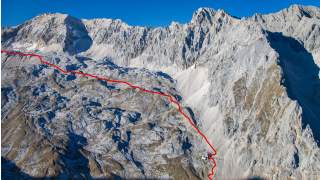 Gebirgslandschaft mit felsigen Gipfeln, über die eine rote Linie einen Wanderweg oder eine Route markiert.