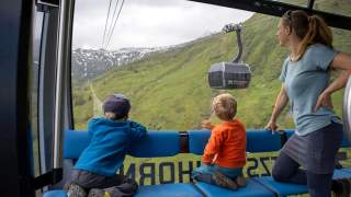 Zwei Kinder und eine Frau schauen aus einer Seilbahnkabine der 3K K-onnection am Kitzsteinhorn runter auf Kaprun.