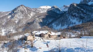 Winterlandschaft mit verschneiten Bergen und einem kleinen Dorf, in dem mehrere Personen Ski fahren.