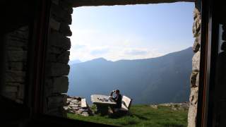 Frau sitzt an Tisch in den Bergen und bereitet Essen zu