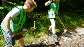 Zwei Personen arbeiten mit Schaufel und Spitzhacke an einem ausgewaschenen Wanderweg.