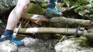 In steinigem Gelände sieht man eine Stufe aus Holz und Stein und die Beine einer Person, die gerade hinaufsteigt.