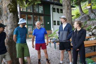 Eine Gruppe Personen steht im Halbkreis am Waldrand vor einem Haus.
