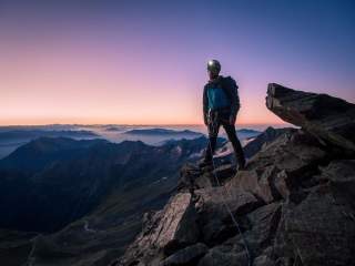 Mann steht auf ausgesetztem Gipfel im Abendlicht