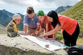 Familie breitet Karte auf Stein in Berglandschaft aus