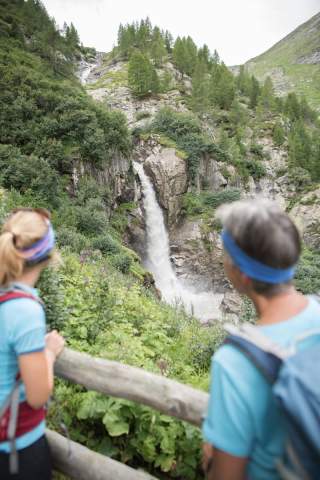 Zwei Menschen blicken auf Wasserfall in den Bergen