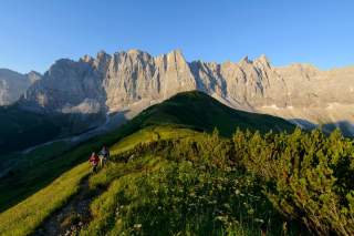 Zwei Menschen wandern auf Bergwiese, im Hintergrund schroffe Berggipfel