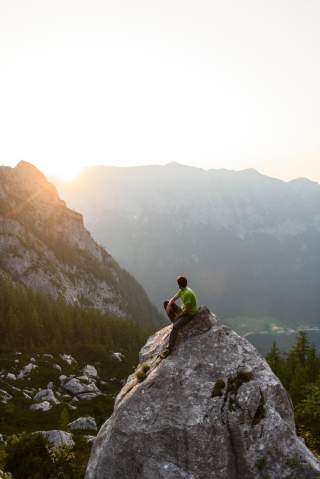 Mensch sitzt auf Fels bei Sonnenuntergang am Berg Mensch sitzt auf Fels bei Sonnenuntergang am Berg