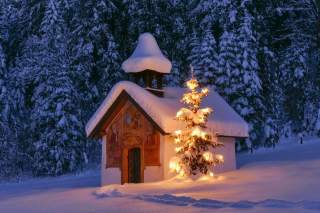 Kapelle in schneebedeckter Landschaft mit beleuchtetem Weihnachtsbaum davor