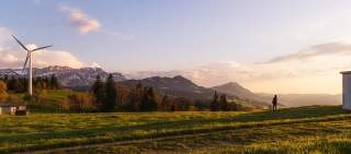 Windrad auf grüner Almwiese vor Alpenkulisse