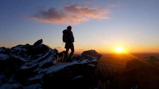 Frau und Hund stehen auf Felsen und genießen den Sonnenuntergang